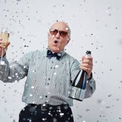 An older man wearing sunglasses holding a bottle of champaign and a glass