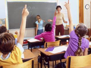 Teacher and rear view of student children with their hands raised in classroom. (Pic: Thinkstock)