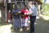 Dr Phil Glatz with two local women in Papua New Guinea who are holding chickens in front of a chicken coop.