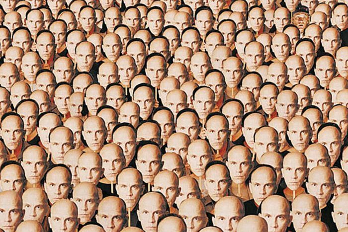 A crowd of people holding up John Malkovich masks to their faces