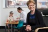 A woman sits on a chair with a child and woman in the background.