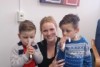 A woman crouches between two boys with plastic tubes in their mouths.