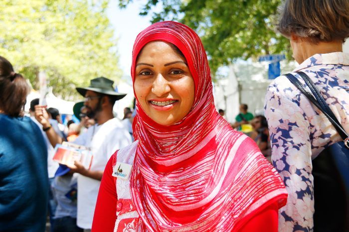 A smiling woman wearing a bright red and silver head scarf.