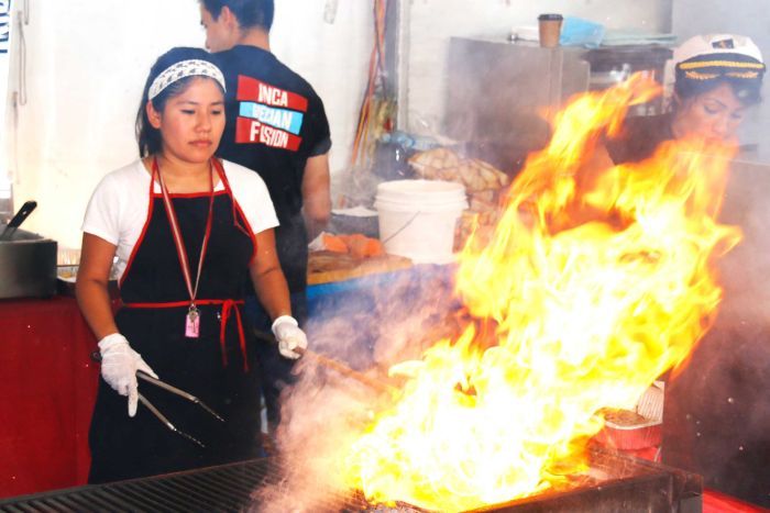 Flames flare up from a barbecue as woman cooks meat.