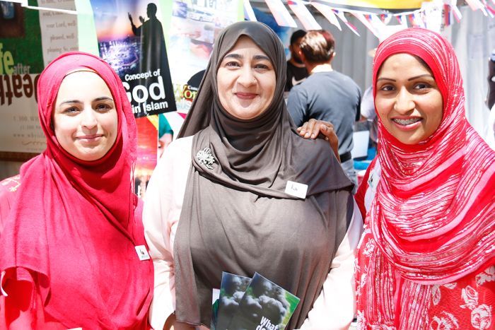 Three women wearing brightly coloured head scarves stand close to each other, smiling. 