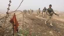 Iraqi Army soldiers walk along a ridge, barbed wire sits in the fore of the image