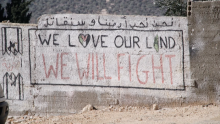 The words "We Love Our Land, We Will Fight" are painted on a grey brick wall in Palestinian village Kafr Qaddum.