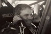 Black and white photograph of Billy Geddes putting his fingers in his ears, sitting in his truck as they test the engine