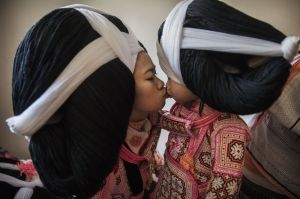 A teenage girl of the Long Horn Miao ethnic minority group kisses her younger sister as they wear headdresses in their ...