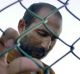 An unidentified Afghan man leans against a chainlink fence of a refugee camp after arriving with other asylum seekers on ...