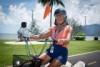 An elderly woman rides a motorised tricycle through parklands in Cairns.