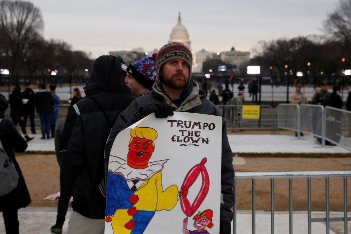 An anti-trump protester holds a sign saying "Trumpo the clown"