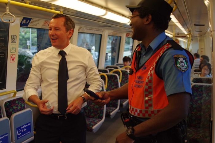 Mark McGowan in a train carriage joking with a train guard who asks to check his ticket