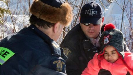 Asylum seeker children are helped into Canada by Royal Canadian Mounted Police officers along the US-Canada border near ...