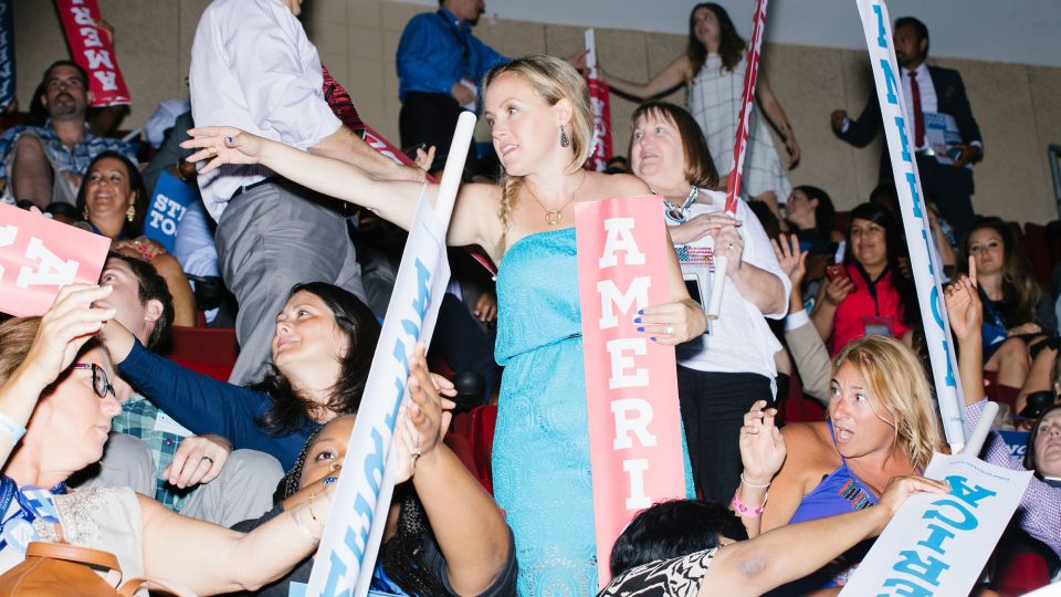 People hold red, white, and blue signs reading "America"