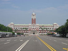 A tall and large building with a tower in its centre. A large road surrounded by trees leads to it.