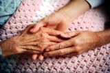 An elderly person's hand is held by a younger person's hands