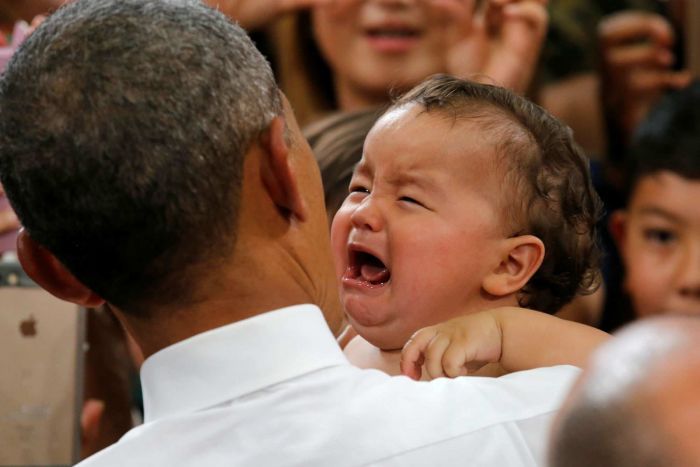 US President Barack Obama holds a crying baby.