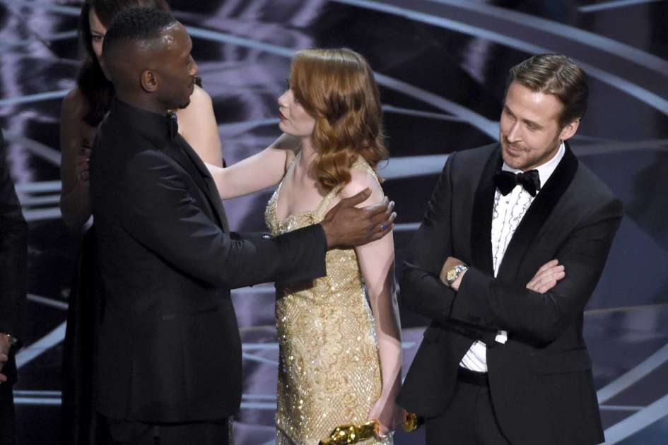 Ryan Gosling, derecha, de pie con los brazos curzados mientras Emma Stone, centro, felicita a Mahershala Ali por el Oscar a la mejor película para "Moonlight" en los Oscar el domingo 26 de febrero de 2017 en el Teatro Dolby en Los Angeles. "La La Land" fue anunciada originalmente como la ganadora pero esto fue coregido y "Moonlight" fue la galardonada. (Foto Chris Pizzello/Invision/AP)