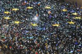 People light the flashes of their mobile phones in the colors of the European Union flag during an anti-government protest demanding the government's resignation, outside the government headquarters, seen at right, in Bucharest, Romania, Sunday, Feb. 26, 2017.