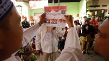 A side profile of a man holding the ballot paper for the election, people in the background look at him. 