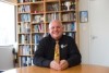 A man sits at a table smiling. Bookshelves in background.