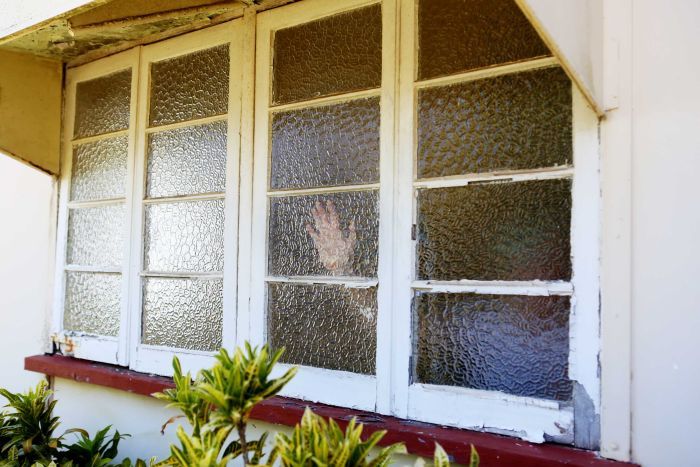 Hand behind glass window of house