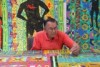 Ted Laxton surrounded by brightly coloured large scale artwork, working on another painting in front of him.