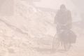 A Syrian man rides his bicycle through smoke and dust after an Assad regime air strike on residential areas of Douma, ...