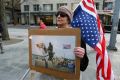 Dianne Reeves, of Seattle, holds an upside-down U.S. flag, commonly seen as a sign of distress, and a photo from the ...