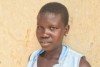 A teenage girl in South Sudan, stands against a brick wall looking into the camera.