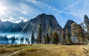 Looking Up from Yosemite Valley at the towering cliffs, as the sun shines though the blue / grey haze of a small ...