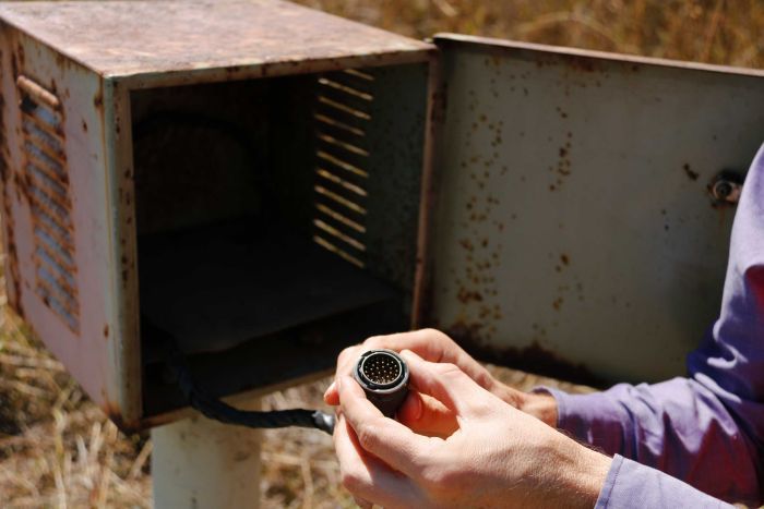 A worker holds a multi-pin connector, attached to a black power cable, inside the metal box.