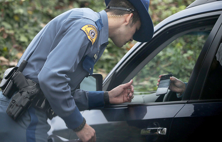 Washington State Trooper Marcus Sanchez looks at a woman’s cell phone after being pulled over for driving with the phone up to her ear, Tuesday, Nov. 22, 2016, in Bellevue. The woman is showing up-to-date insurance information, stored on the phone, and was not cited because she said the conversation was on speaker phone.