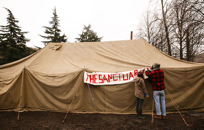 Emily Thompson, left, and Cory Potts help put up a sign, which reads ‘The Sanctuary,’ at the homeless camp on state land near Royal Brougham Way South and Airport Way South Sunday, March 5, 2017.