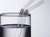 Close-up of two straws in a glass of water. The straws appear bent owing to the refraction of light.