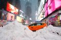 A taxi drives past piles of snow as a storm sweeps through Times Square on Tuesday.)