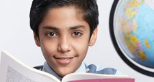 Young boy with an open book looking at the camera and a globe at his side (East India, asian, student, education).