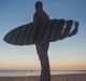 A surfer pauses at the water's edge, looking out to the ocean's movement, assessing the changing atmosphere and the ...