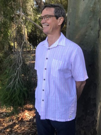 A mid-shot of Mike Nahan smiling and standing in front of a tree.