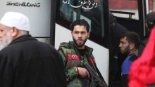 An militant shouldering an automatic rifle prepares to board a bus.