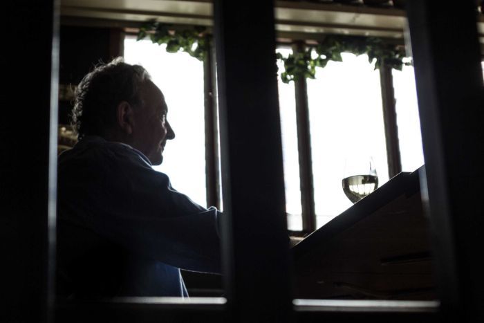 Playwright Louis Nowra sits at a table, holding a glass of wine