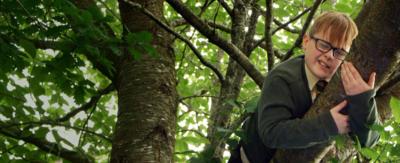 A boy closes his eyes while lying on a tree branch.