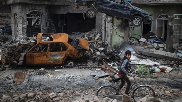 A boy rides his bike past destroyed cars and houses in a neighbourhood recently liberated by Iraqi security forces, on ...