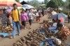 People walk past sweet potatoes laid out on the ground at a colourful market