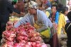 Bright red sweet potatoes in the foreground, while a Papua New Guinea woman sorts them in the background.