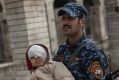 A federal police officer carries an injured boy through a destroyed train station during fighting between Iraqi security ...