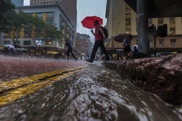 Dark skies loom over the Brisbane CBD as pedestrians walk near flowing water