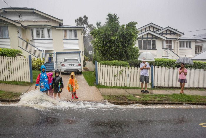 A family plays in the rain outside a home from ex-cyclone Debbie in Newmarket.