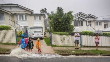 A family plays in the rain outside a home from ex-cyclone Debbie in Newmarket.